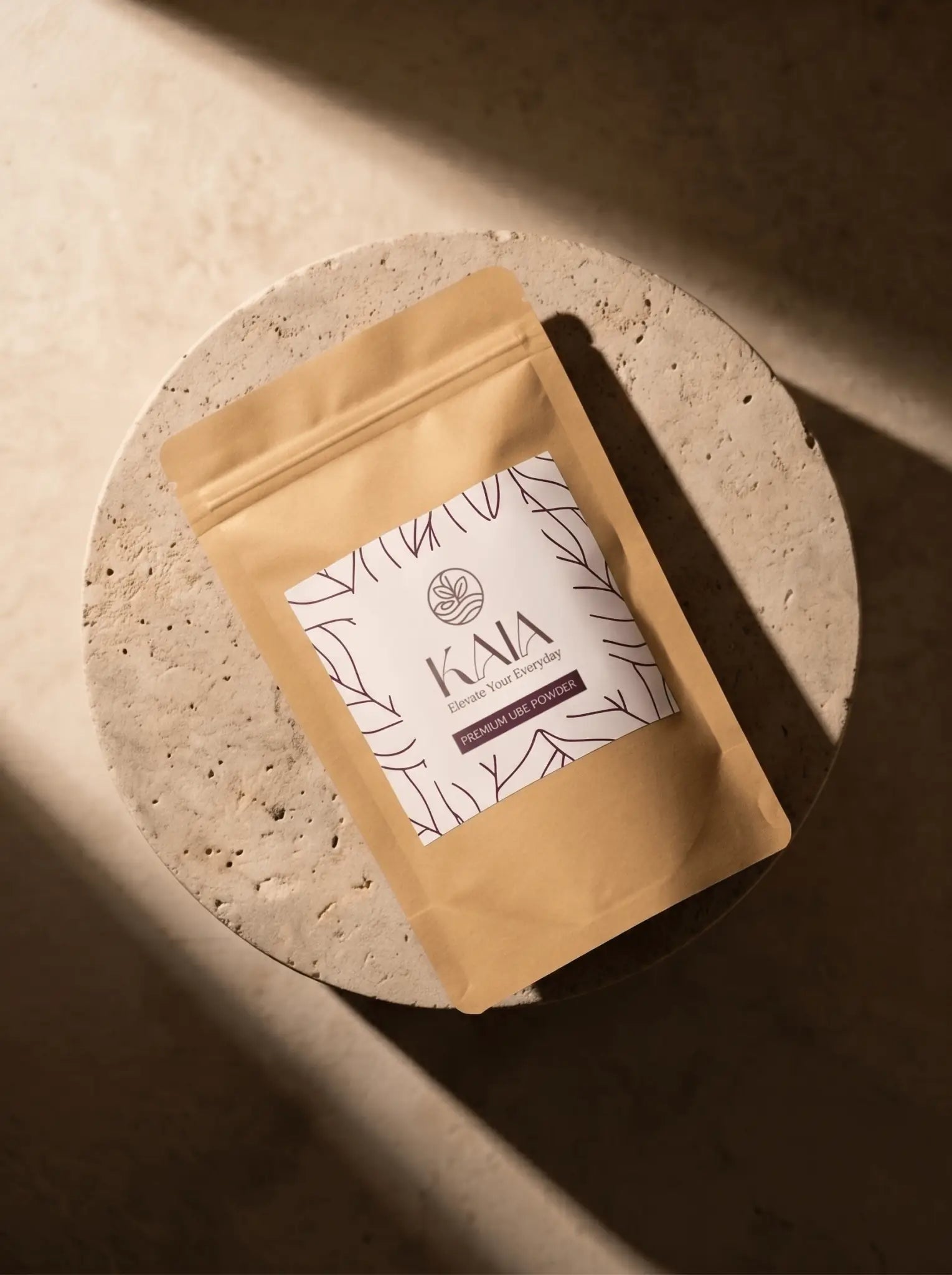 Top-down view of KAIA Origin premium ube powder 100g pouch on round travertine surface, Belgian freeze-dried purple yam

